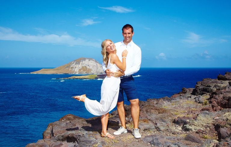 Hawaii Weddings at Makapuu Pt. Lookout A couple embraces on a rocky cliffside with a blue ocean and island in the background at Makapuu Pt. Lookout.